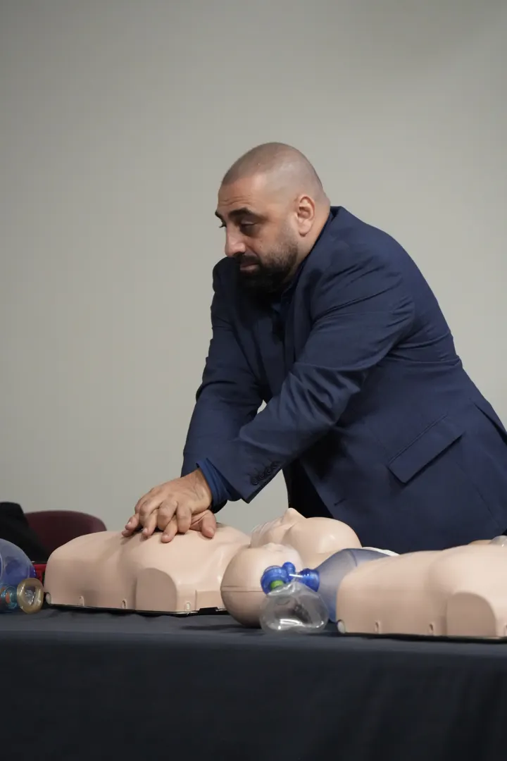 A man in a suit doing chest compressions on a CPR manikin
